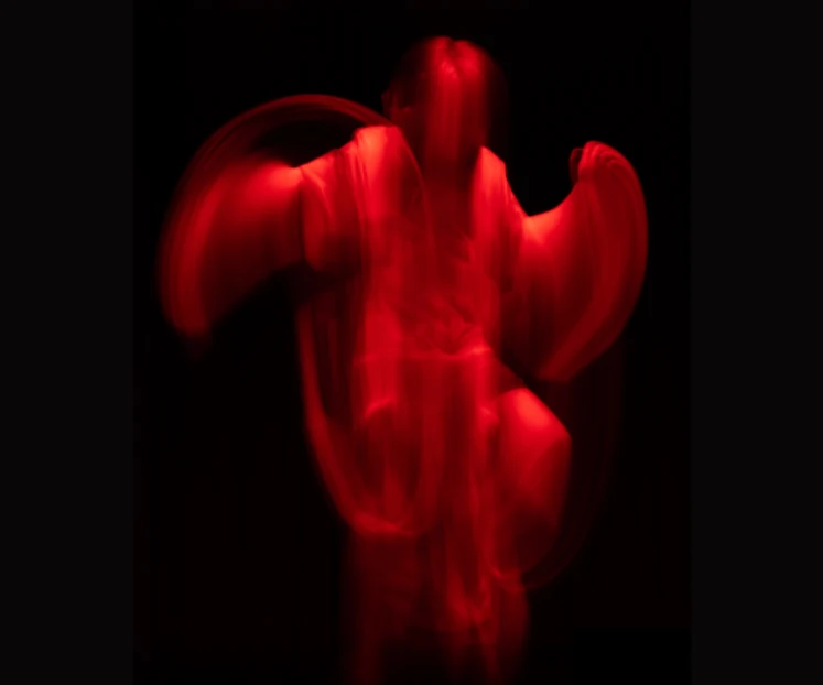 A blurred boy who looks red and in movement against a black background, from the digital art video Threshold